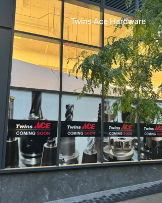 Outside of building with Twins Ace Coming Soon Poster, tree in the corner.