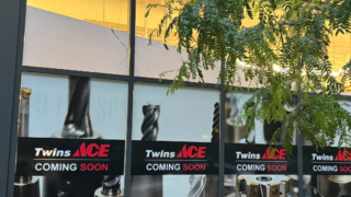 Outside of building with Twins Ace Coming Soon Poster, tree in the corner.
