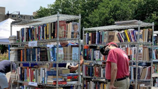 Multiple bookshelves at outdoor shopping center for used book sale; man looking at books.